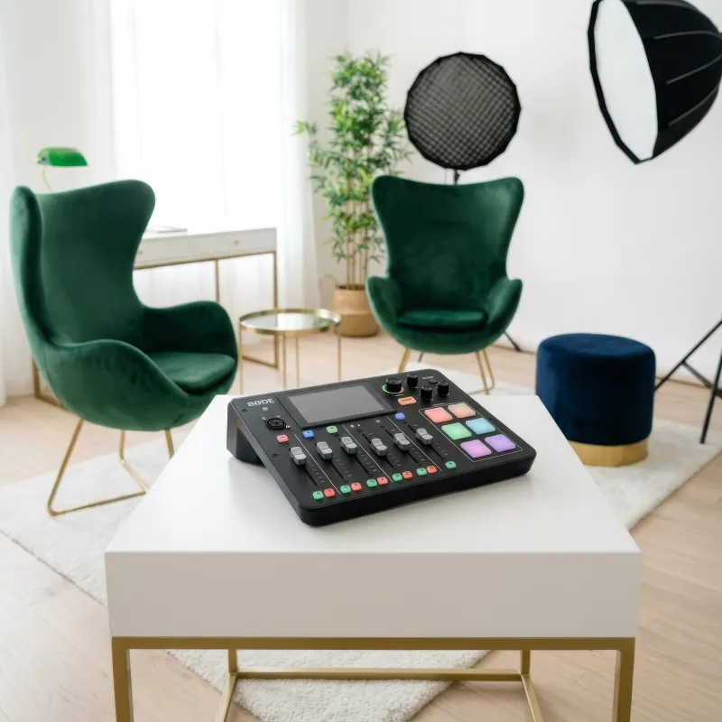 La console RØDECaster Duo posée sur une table blanche à cadre doré, dans un salon blanc aux fauteuils de velours vert (création visuelle)